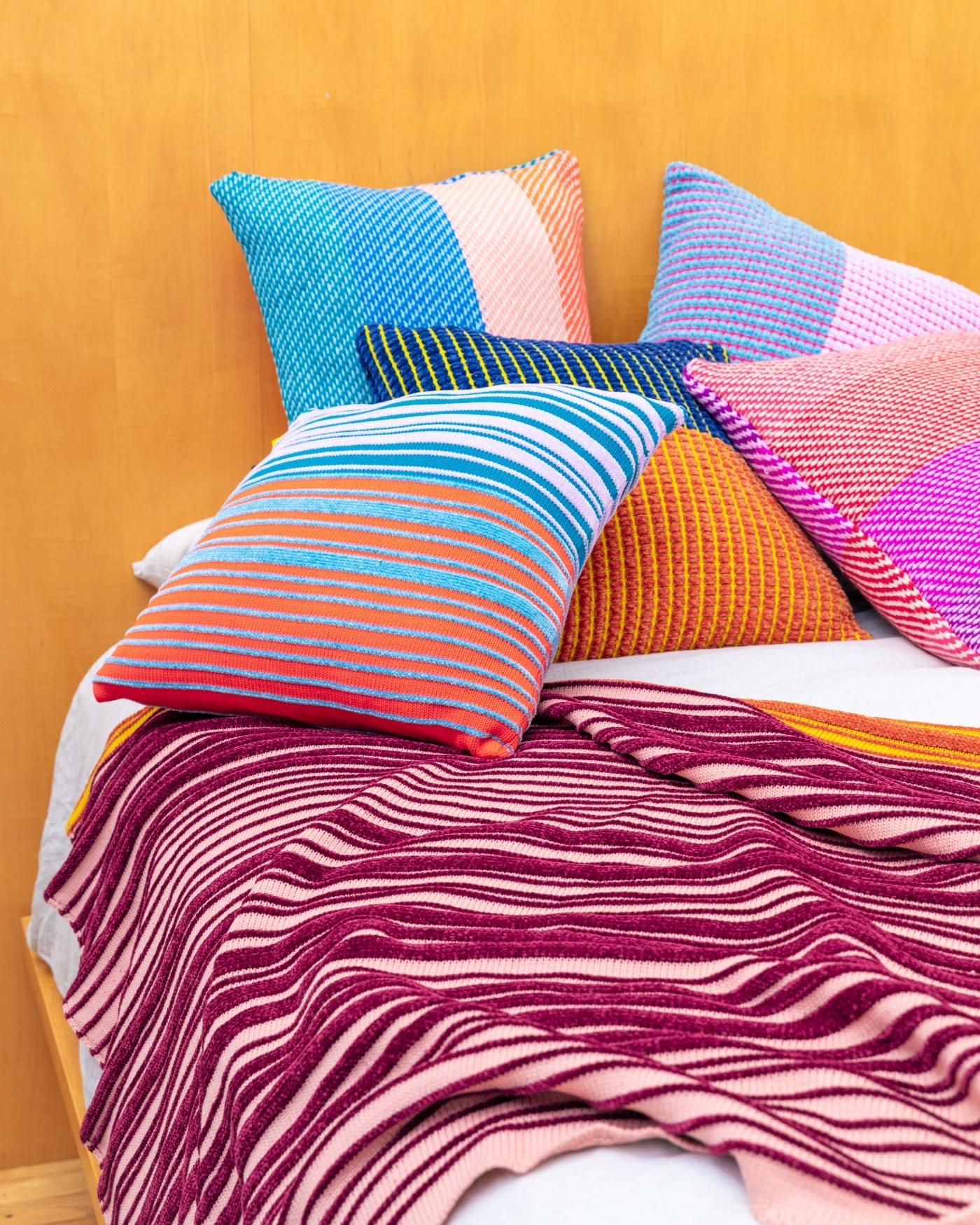 colorful striped knit throw and deadstock chenille pillows on bed