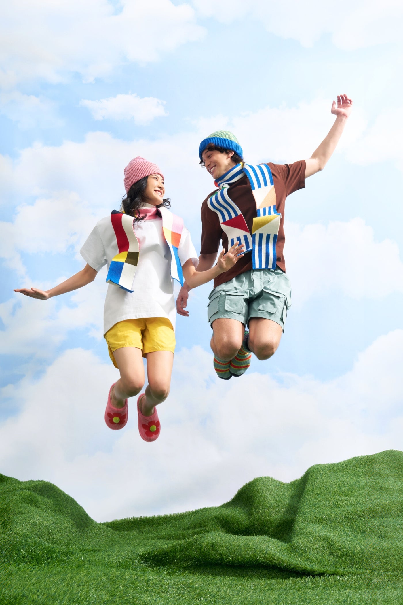 two models jumping in the air wearing skinny knit scarves and bright beanies