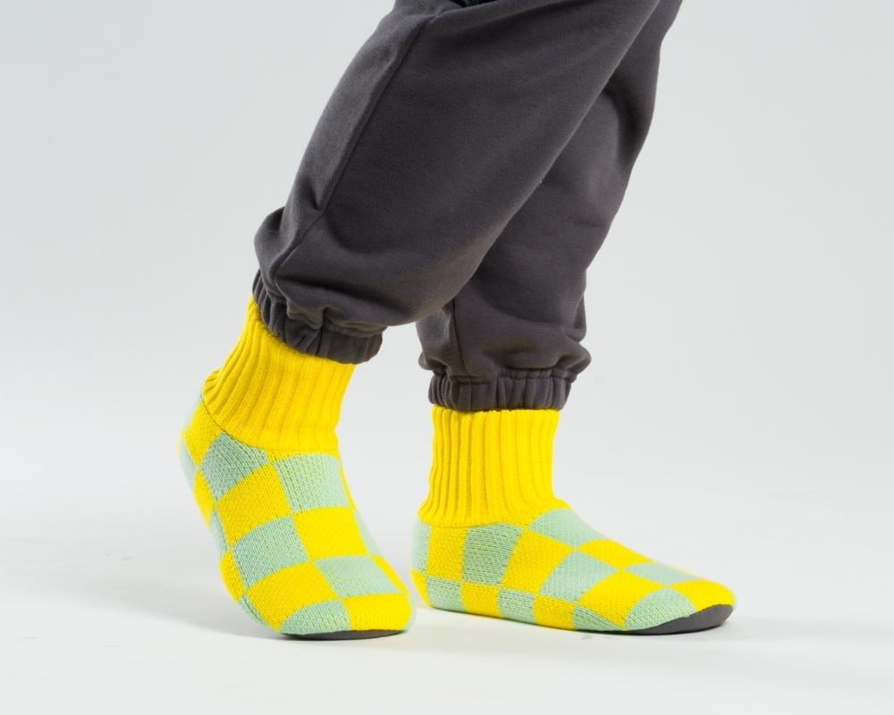 person's feet walking in yellow and teal checkerboard sock slippers