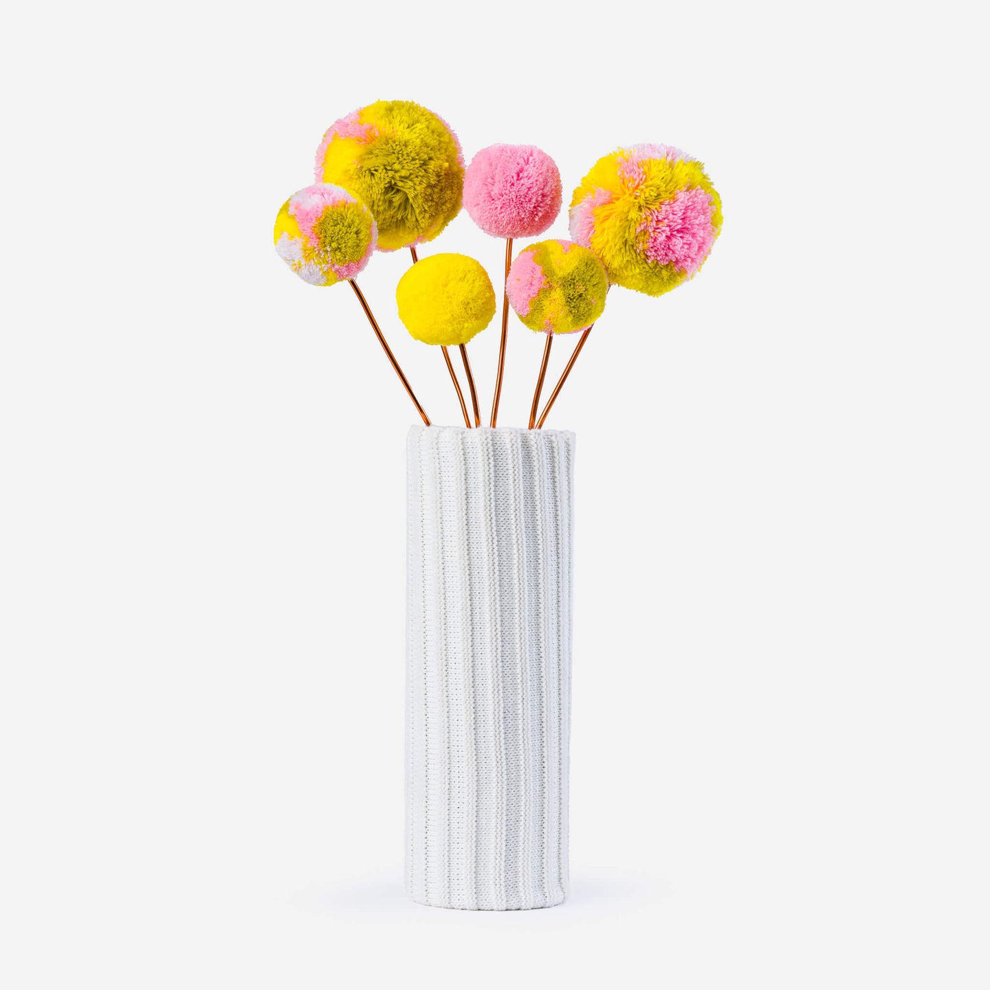 colored pom pom flower bouquet in a knitted vase with a white background