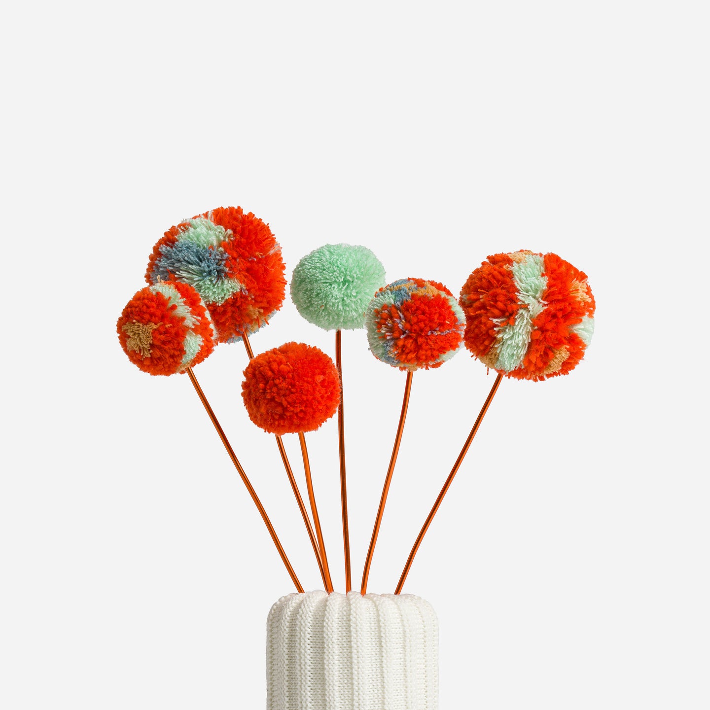 pretty and colorful pom pom flowers in a knitted vase with a white background