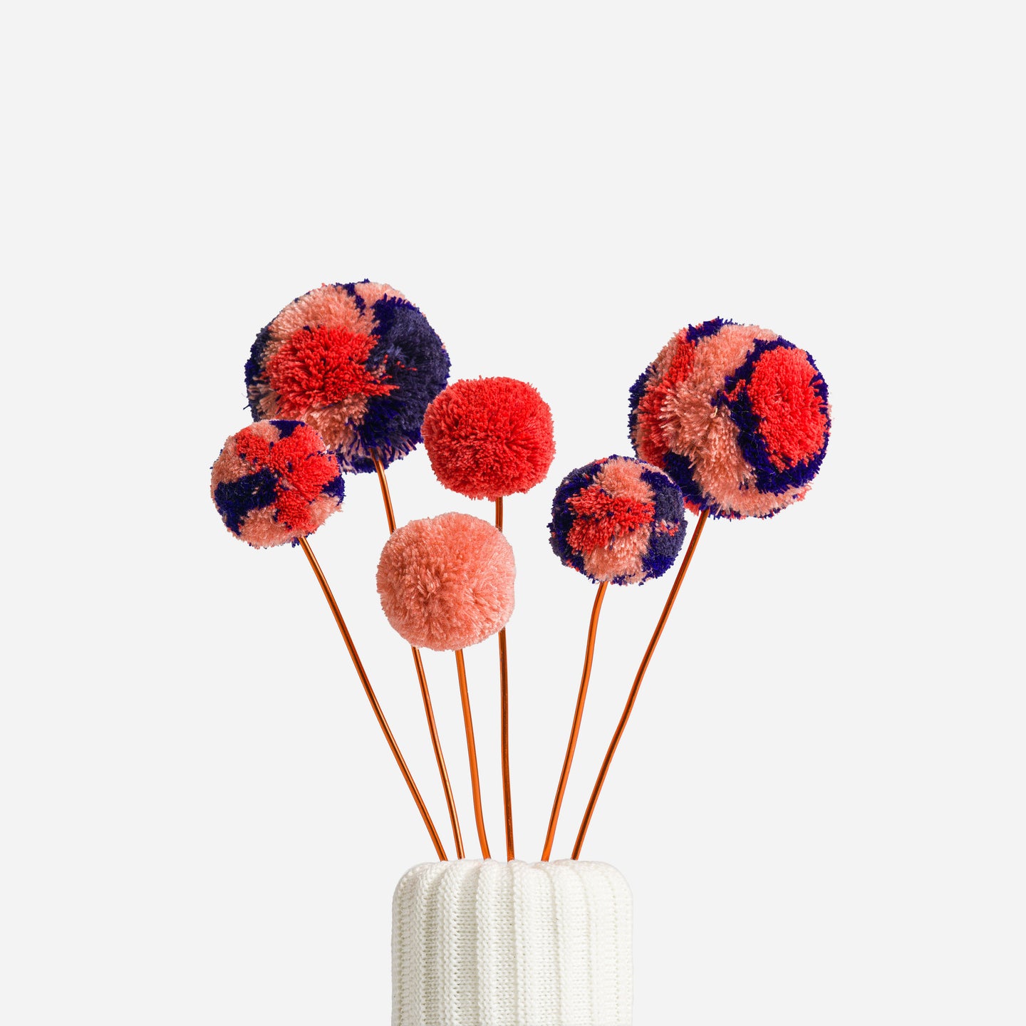 colored pom pom flower bouquet in a knitted vase with a  white background